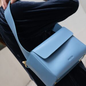 Premium leather bag by Bartin held as shoulder bag with long strap by woman in blue dress.