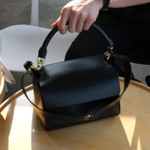 a classy functional black leather handbag help over a wooden table in a bangkok cafe