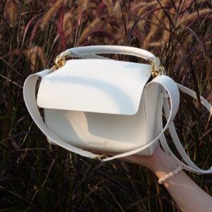 hand holding premium white leather cross body and handbag in front of a field