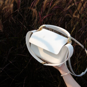 hand holding a white leather handbag in front of a field