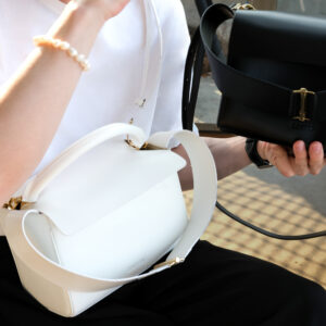 man holding two luxury leather bags. One is a white handbag and the other a black leather handbag with crossbody strap showing