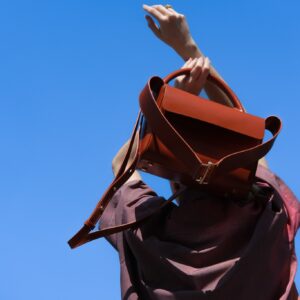 lady holding leather handbag behind her head whilst looking at the sky