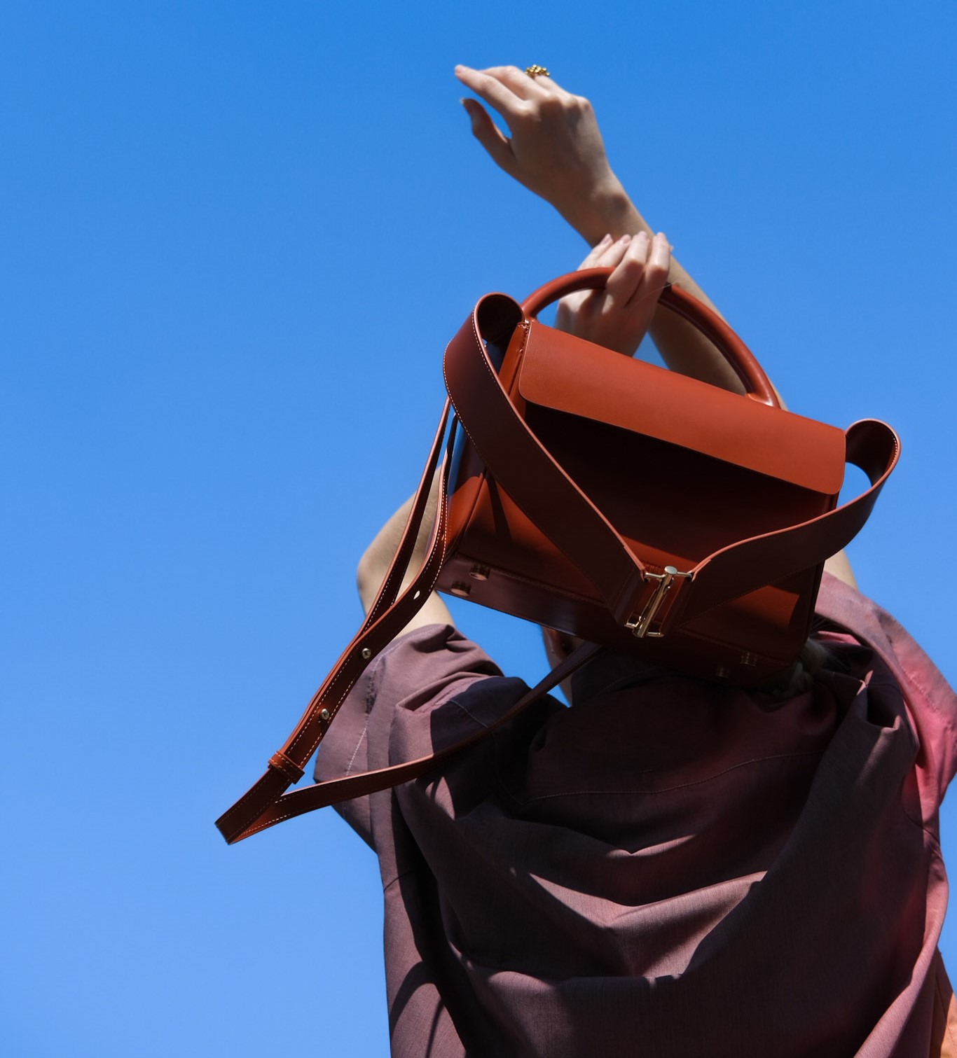 lady holding leather handbag behind her head whilst looking at the sky